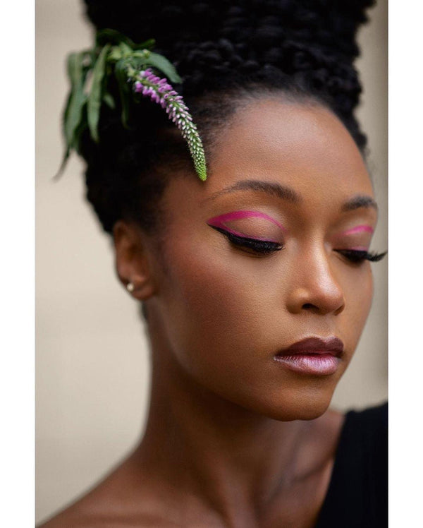 Model wearing bold, vibrant pink UV vegan paint liner in a precise graphic wing style on eyelids.