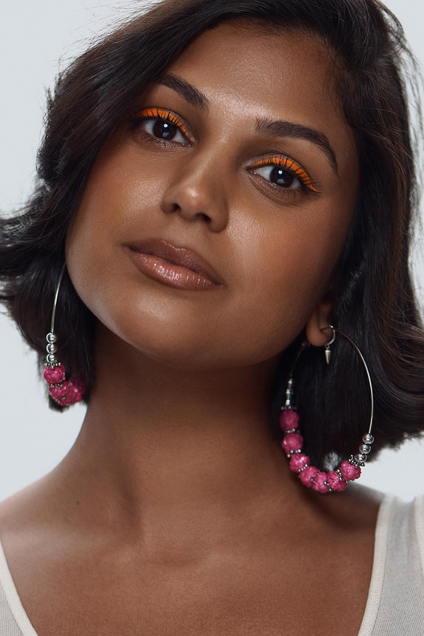 Model with dark hair wearing vibrant orange UV vegan paint eyeliner and large pink beaded hoop earrings.