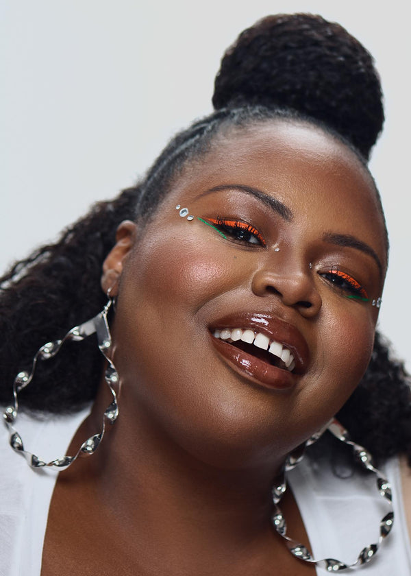 Model wearing vibrant orange and green UV vegan paint liner with face gems and glossy lips.